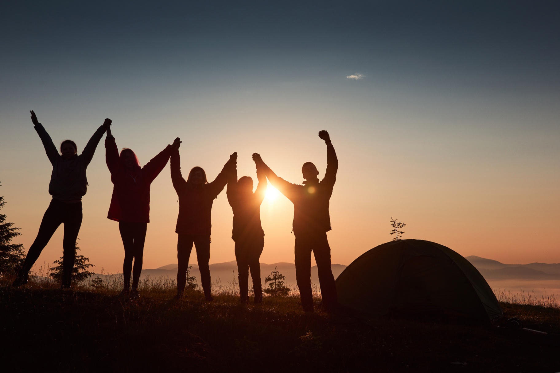 Grupo de amigos celebrando al atardecer junto a una tienda de campaña
